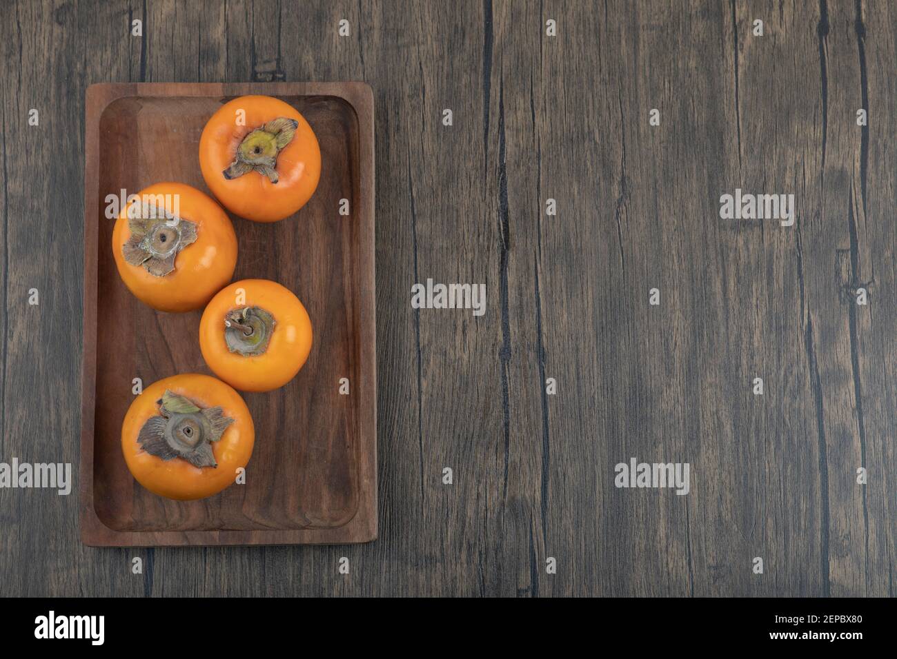 Plate of tasty fuyu persimmon fruits on wooden surface Stock Photo