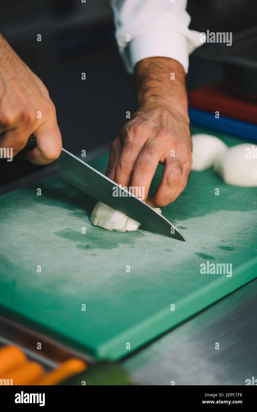 professional chef slicing onions over a green board in the restaurant ...