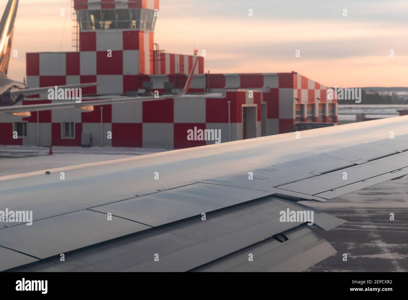 airport building at dawn on the runway with flashing beacon painted in red and white checkerboard squares. airplane window view Stock Photo