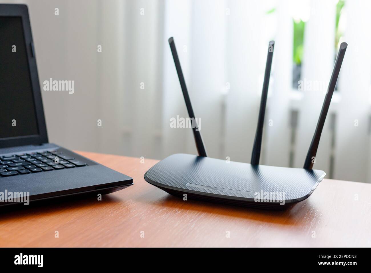 wireless wifi router and laptop at wooden table indoors. window behind