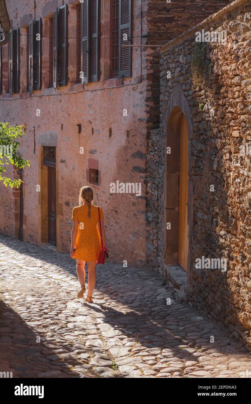 A young female tourist in a summer dress explores a country lane in the quaint and charming medieval French village of Conques, Aveyron Occitanie Fran Stock Photo