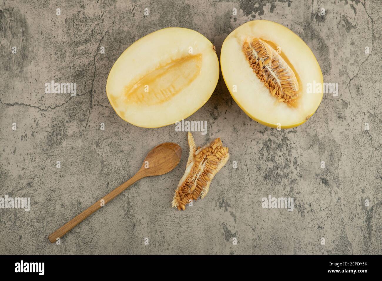 Halved delicious yellow melons on marble surface with wooden spoon aside Stock Photo