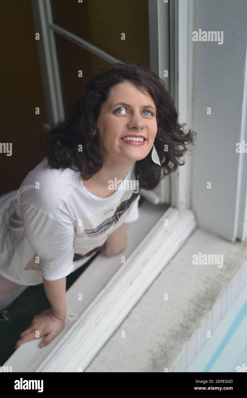 woman looking delighted out of the window into the sky as symbol for a relationship with God or expecting good things to come or just happiness Stock Photo