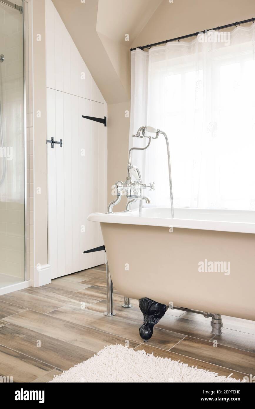 Retro bathroom interior design with cast iron roll top bath, clawfoot or claw foot bath tub. Contemporary, luxury bathrooms with floor tiles, UK Stock Photo