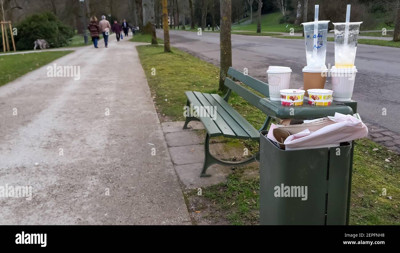 Park bench and garbage bin  full with dish from take away drinks, ice cream and eating outdoors. Socializing, meeting in the park during lock down. Stock Photo