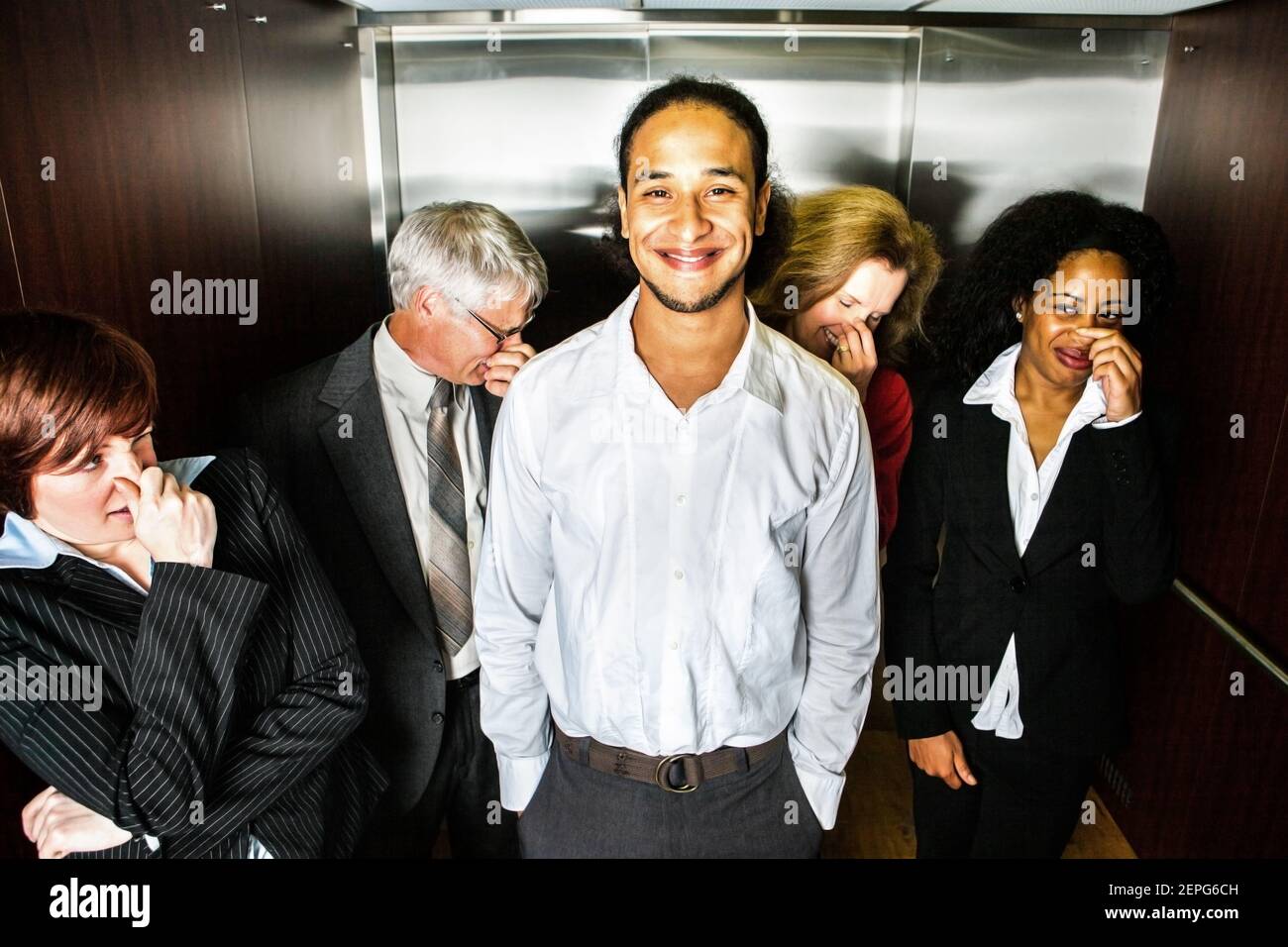 A young man smiles in embarrassment in an elevator while people hold their noses. Stock Photo