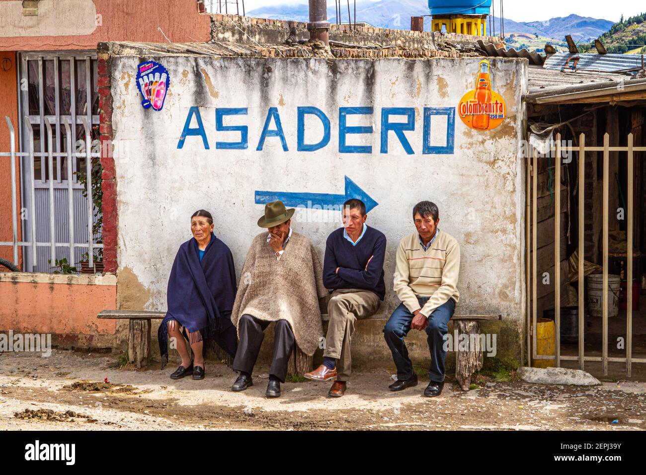 1 dog,Colombian 3 men, 1 women sitting on bench, waiting. 1 in traditional hat  poncho, Ruana. Asadero sign Boyacá Department, Colombia, South America Stock Photo