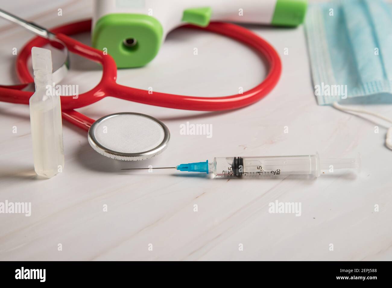 The doctor's equipment consists of a syringe with a coronavirus vaccine, an infrared thermometer, a stethoscope and a medical mask. Stock Photo