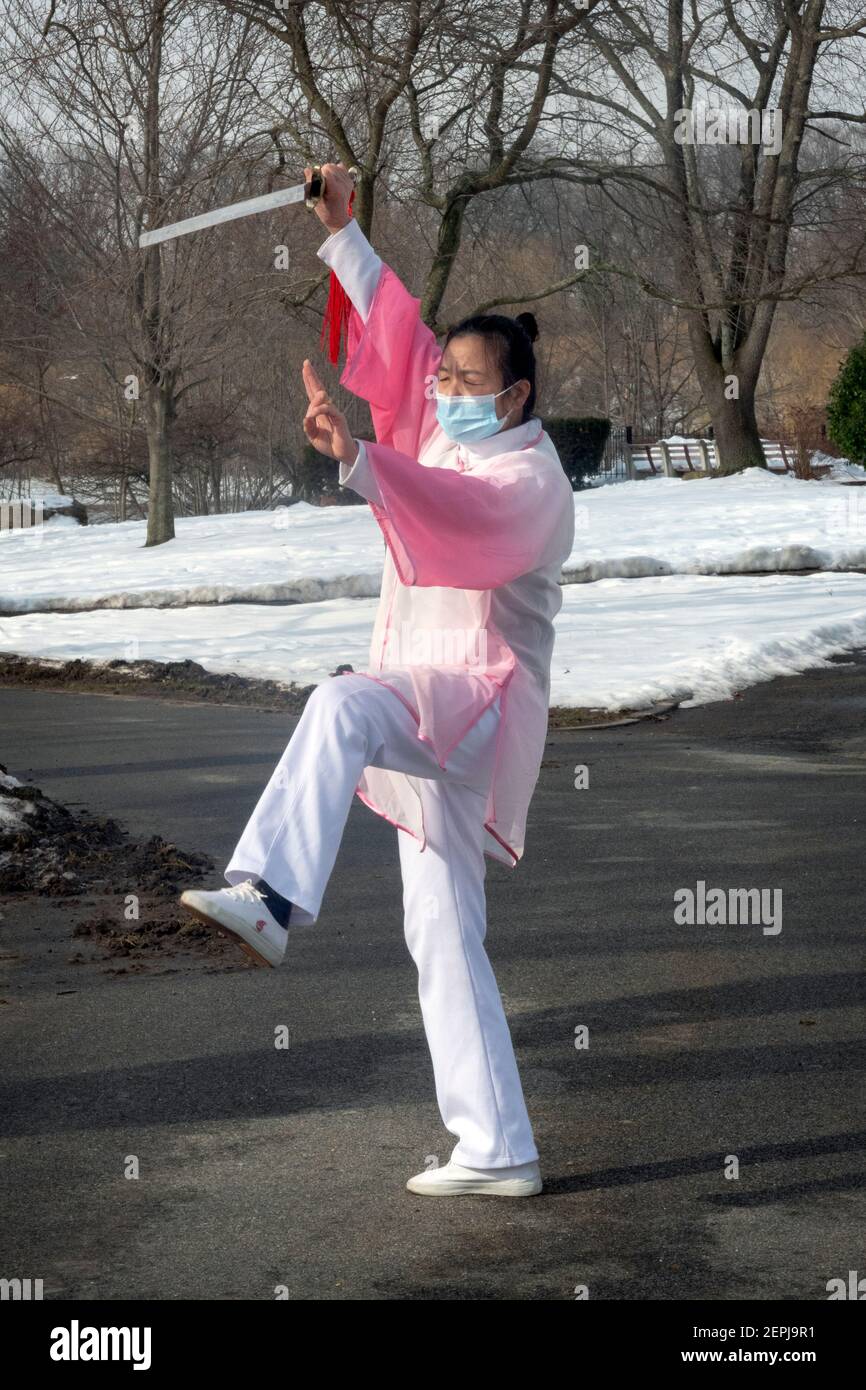 A middle aged Chinese American woman gracefully does Tai Chi dance exercises with a sword in a park in Flushing, Queens, New York City. Stock Photo