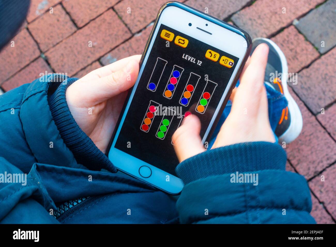 Looking down at a child's hands playing a game on an iPhone smartphone. Stock Photo