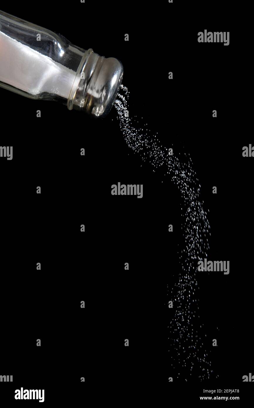 A salt shaker with salt pouring out on a black background. Stock Photo