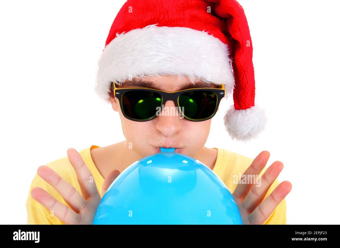 Young Man in Santa Hat and Sunglasses inflate a Blue Balloon on the White Background closeup Stock Photo