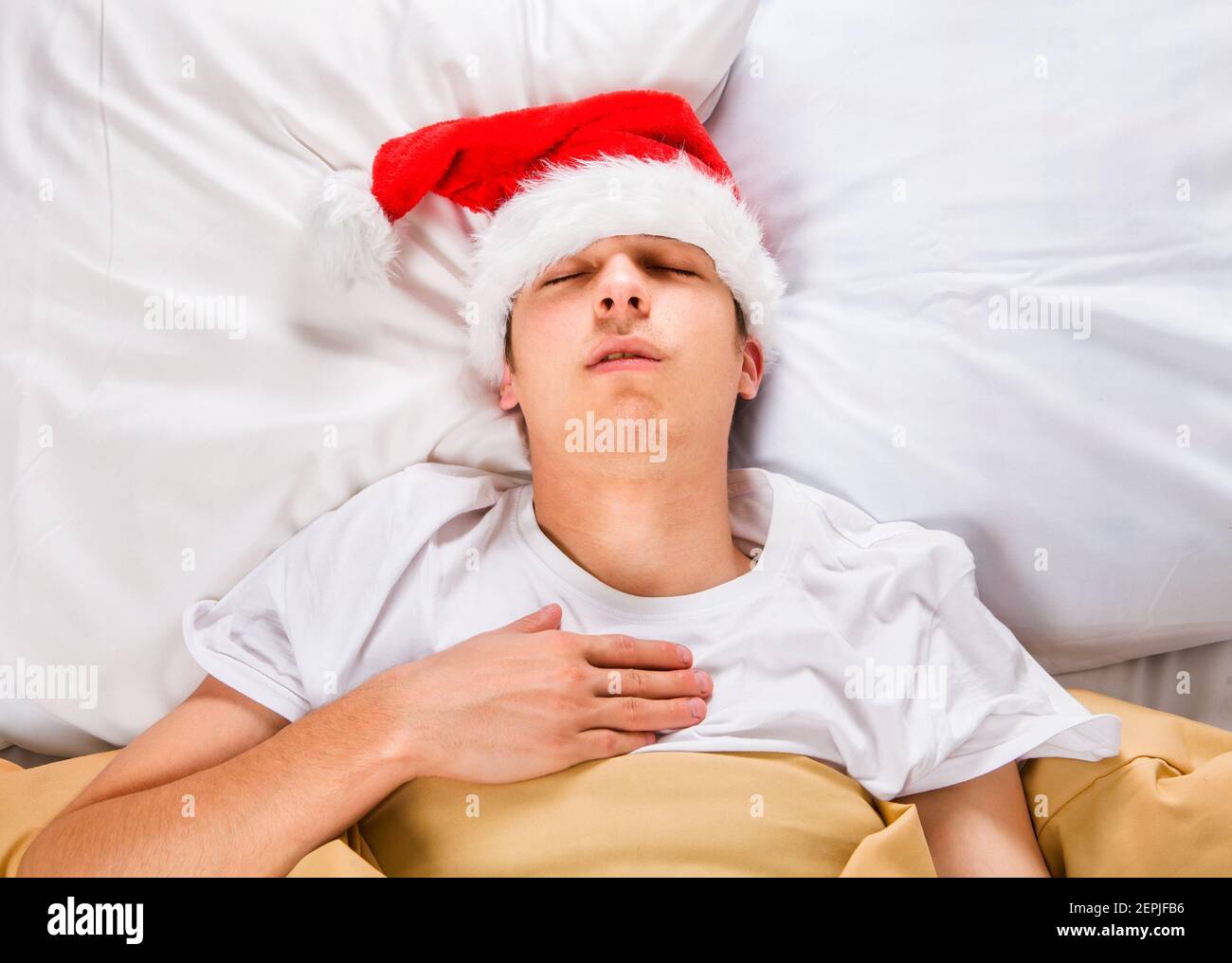 Very Tired Young Man in Santa Hat sleep in the Bed at the Home Stock Photo