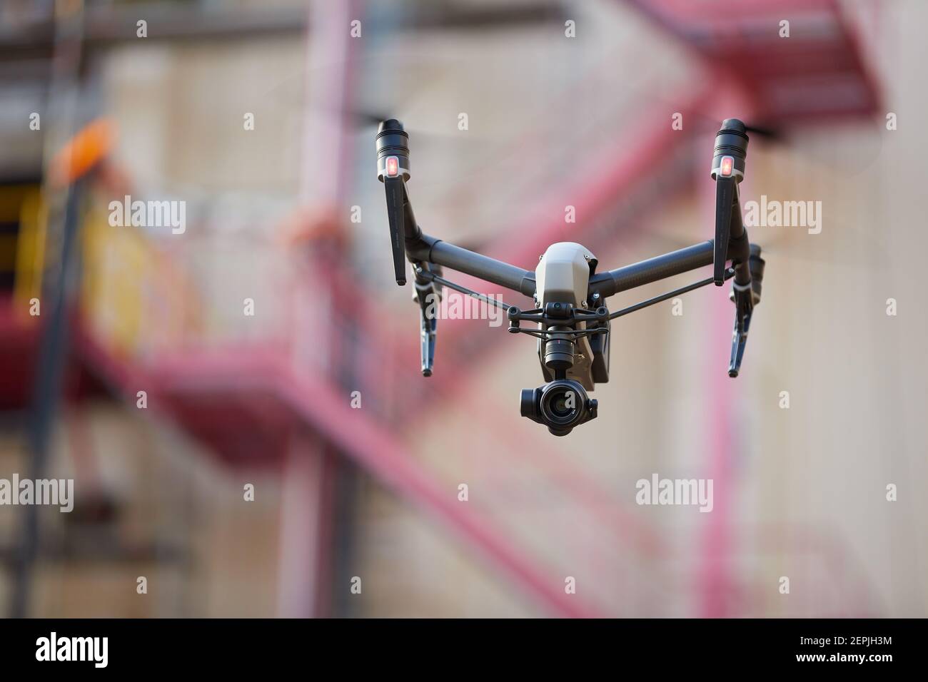 Hovering  black quadcopter with  powerful camera against blurred iindustrial construction. Visual inspection in industry. Stock Photo