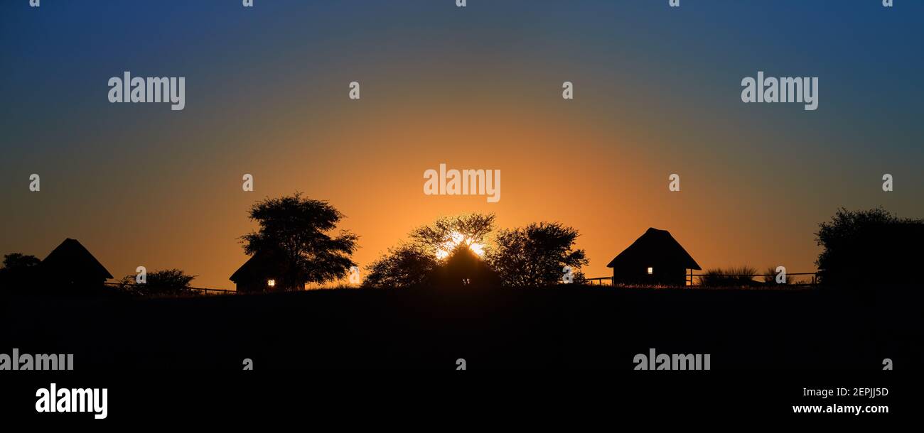 Silhouette of african village on horizon against morning orange-blue sky and rising sun. Calm african landscape, Kalahari, Botswana. Stock Photo