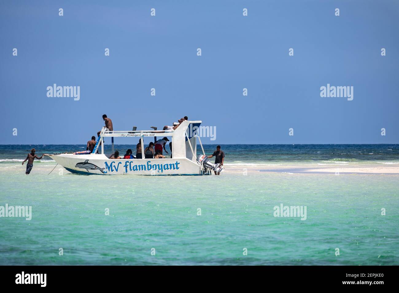 A glass bottom boat moored by a low tide sand bank with people on the sand, Diani, Kenya Stock Photo