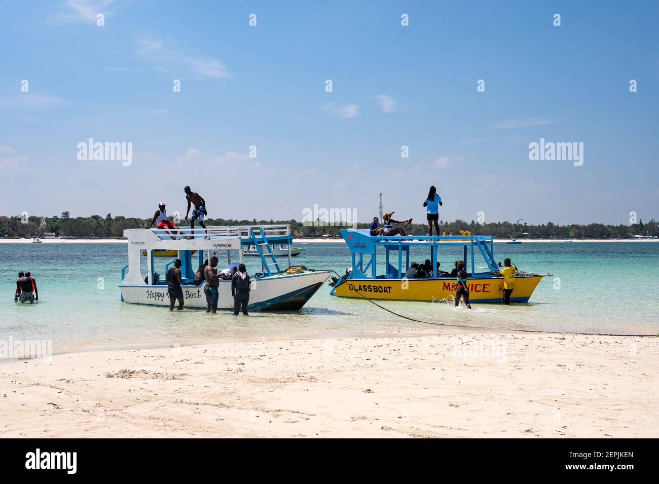 Glass bottom boats moored by a low tide sand bank with people on the beach, Diani, Kenya Stock Photo