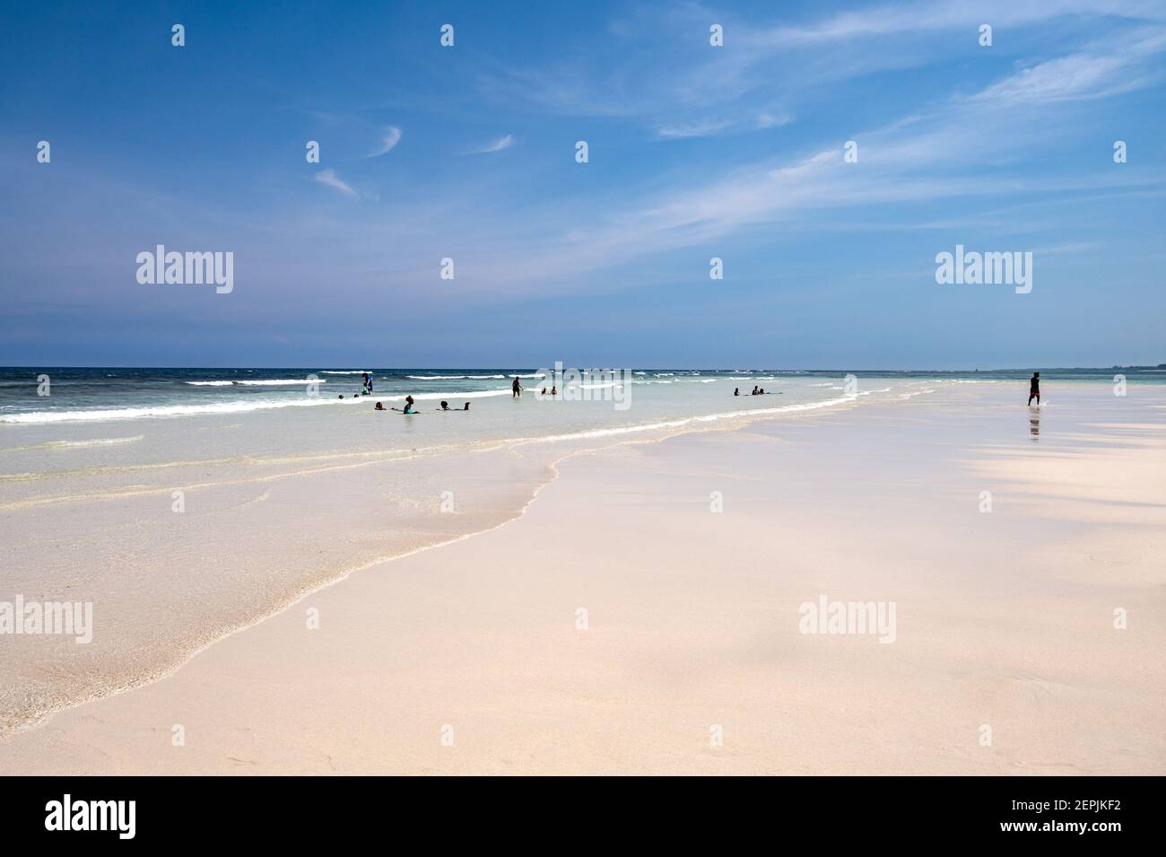 A stretch of sand bank exposed at low tide with tourists at the shoreline, Diani, Kenya Stock Photo