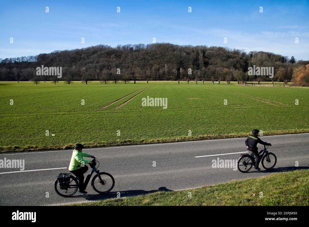 Fahrradfahrer auf einer zweispurigen Landstrasse vor einem Feld. Im Hintergrund befindet sich ein bewaldeter Huegel. Es ist Winter. Stock Photo
