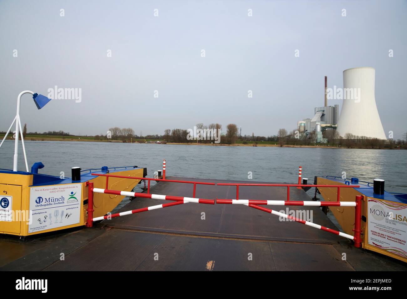 Blick von der Rheinfaehre nach Orsoy auf des Kohlkraftwerk Duisburg Walsum. Im Vordergrund ist die rot, weisse, Absperrschranke der Faehre zu sehen. Stock Photo