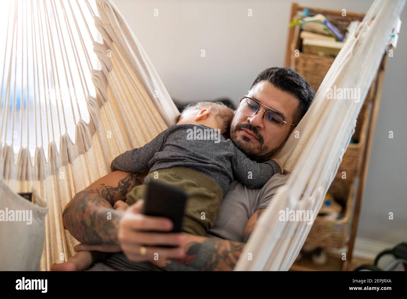 Man checking his phone while his little baby son is sleeping Stock Photo