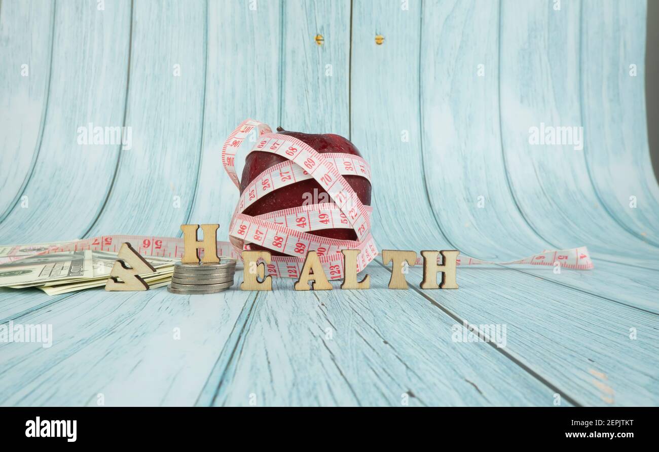 Fitness, Healthy Concept. Red apple with measuring tape isolated on blue background . Diet. Dietary nutrition. Text health replacing wealth. Selective Stock Photo