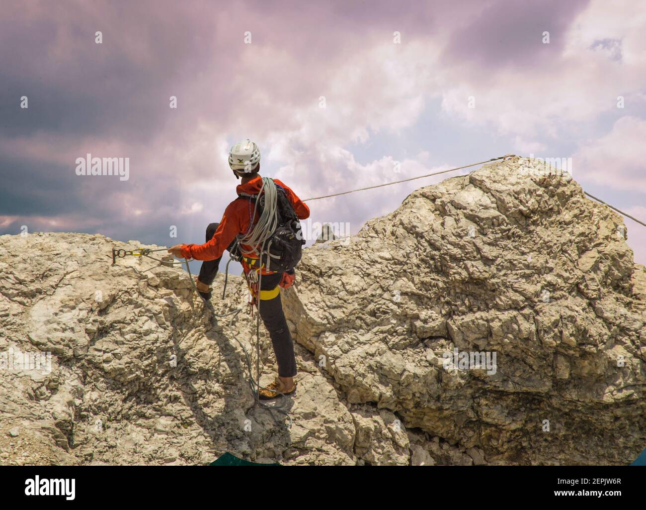 A Rock Climber in a red jacket with his ropes and climbing gear Surveys