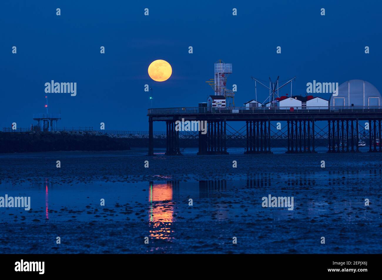Herne Bay, Kent, UK. 27th February 2021: UK Weather. Full snow moon just Waning Gibbous rises into a clear sky over Herne Bay pier at the end of a fine day, during the blue hour after sunset. Credit: Alan Payton/Alamy Live News Stock Photo