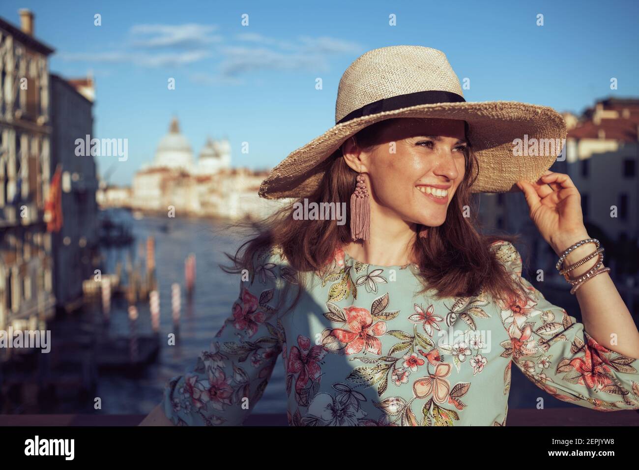 smiling elegant solo traveller woman in floral dress with hat having walking tour on Accademia bridge in Venice, Italy. Stock Photo