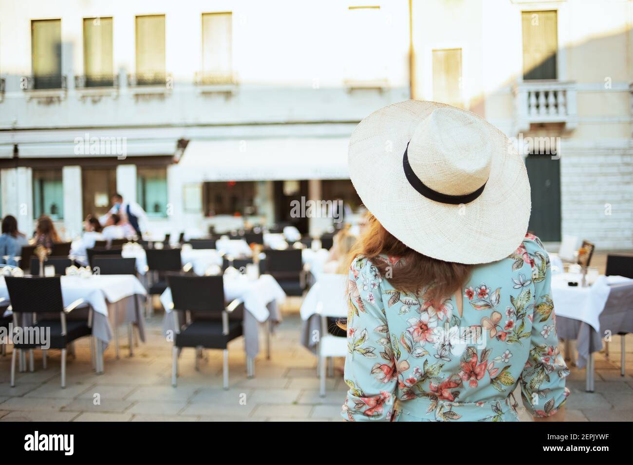 Seen from behind trendy solo traveller woman in floral dress with hat exploring attractions in Venice, Italy. Stock Photo