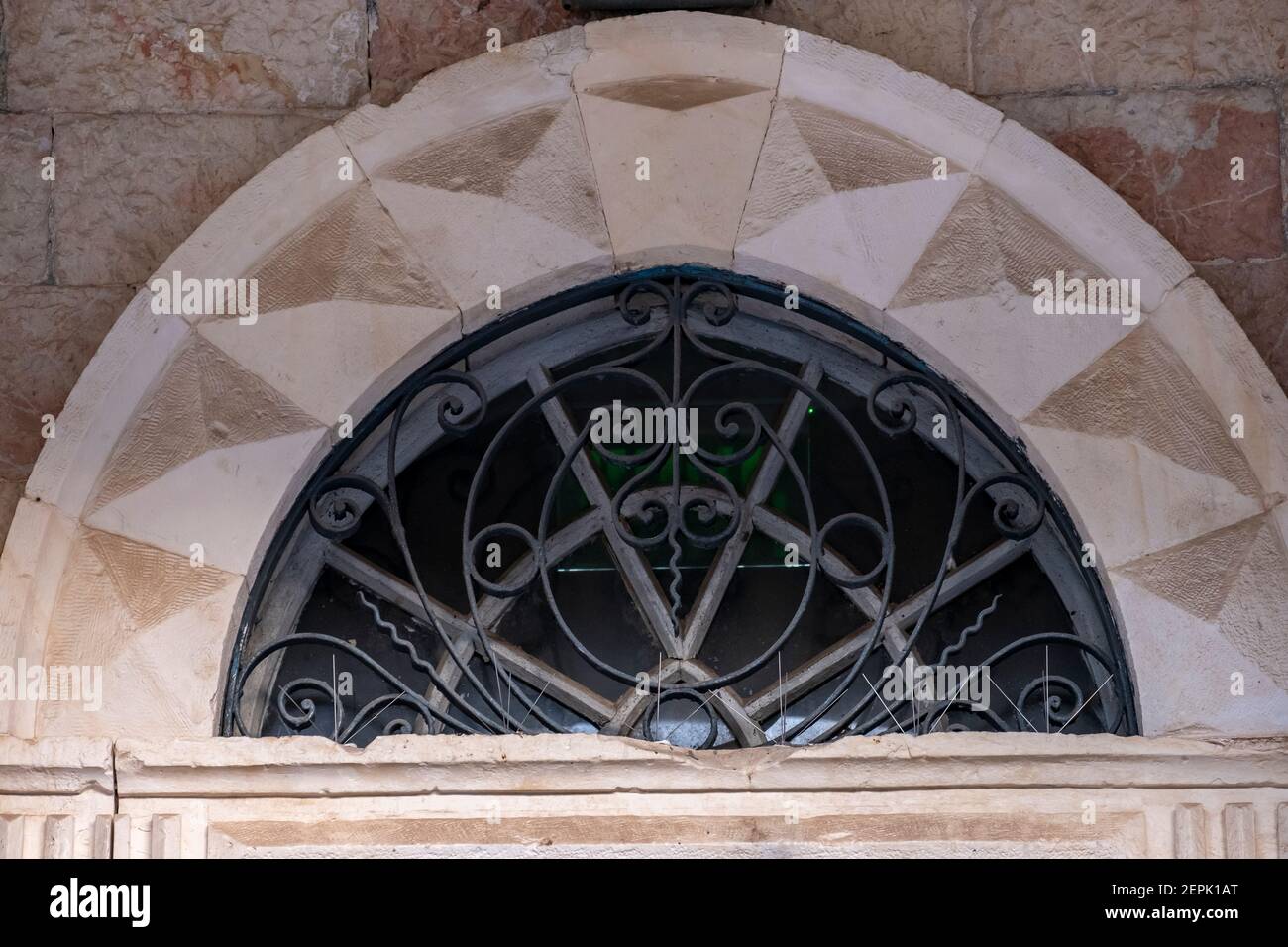 An elaborately semi-circular upper window, with a stylized iron grille ...