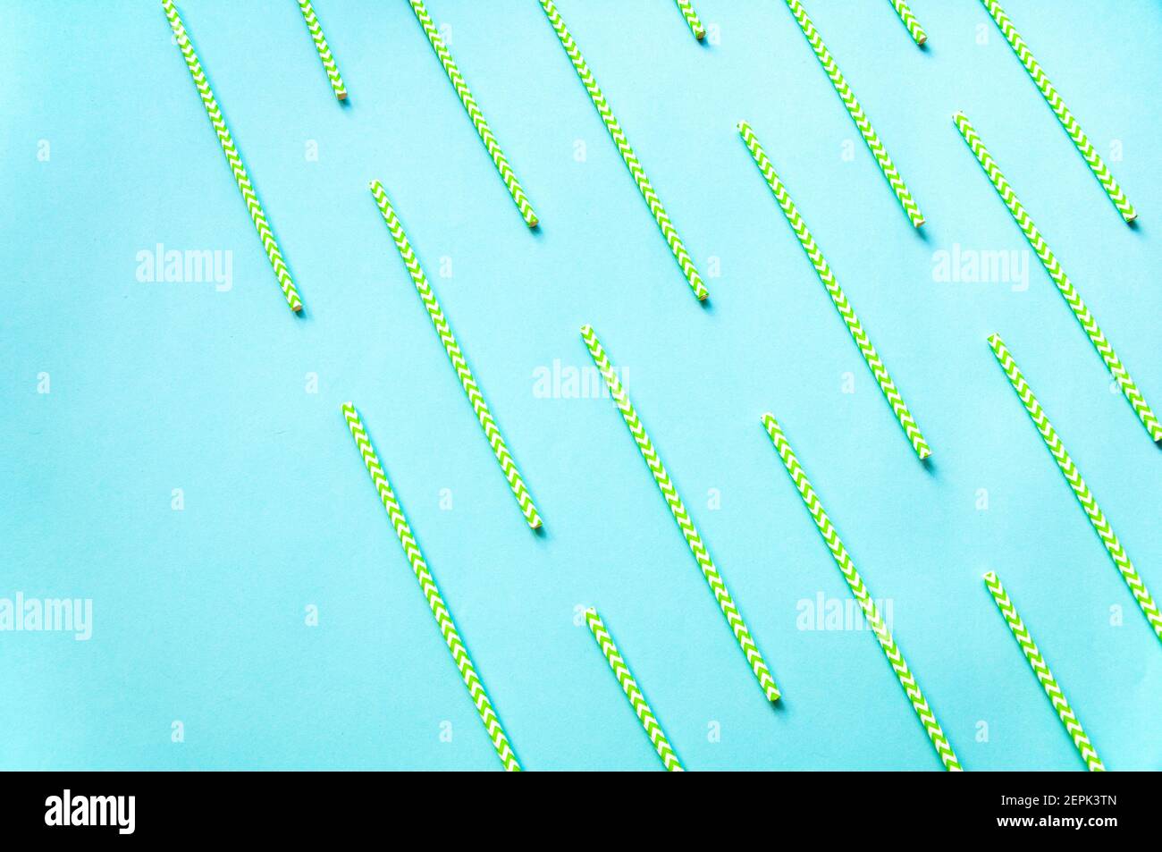 disposable green and white straws are laid out on a background of blue paper Stock Photo