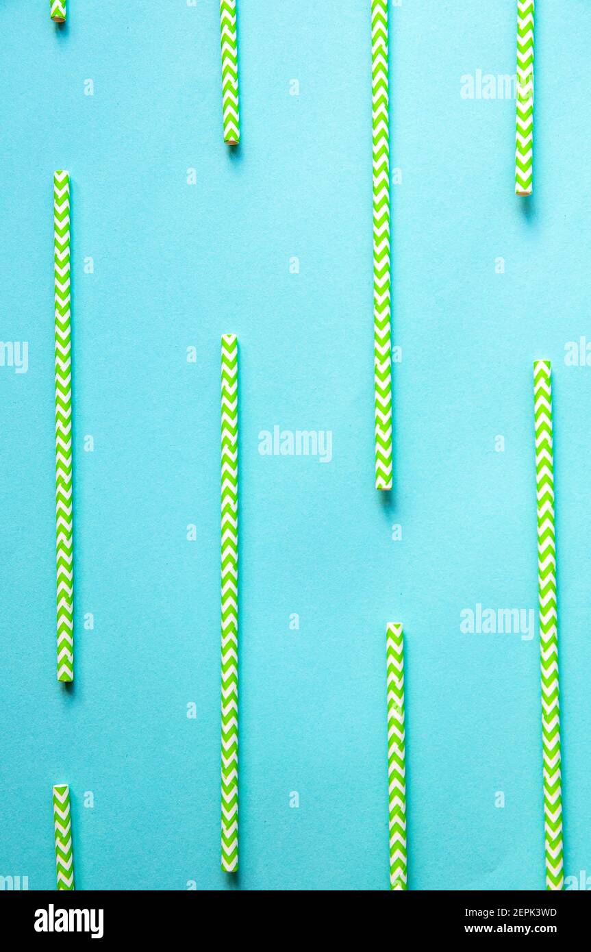 disposable green and white straws are laid out on a background of blue paper Stock Photo