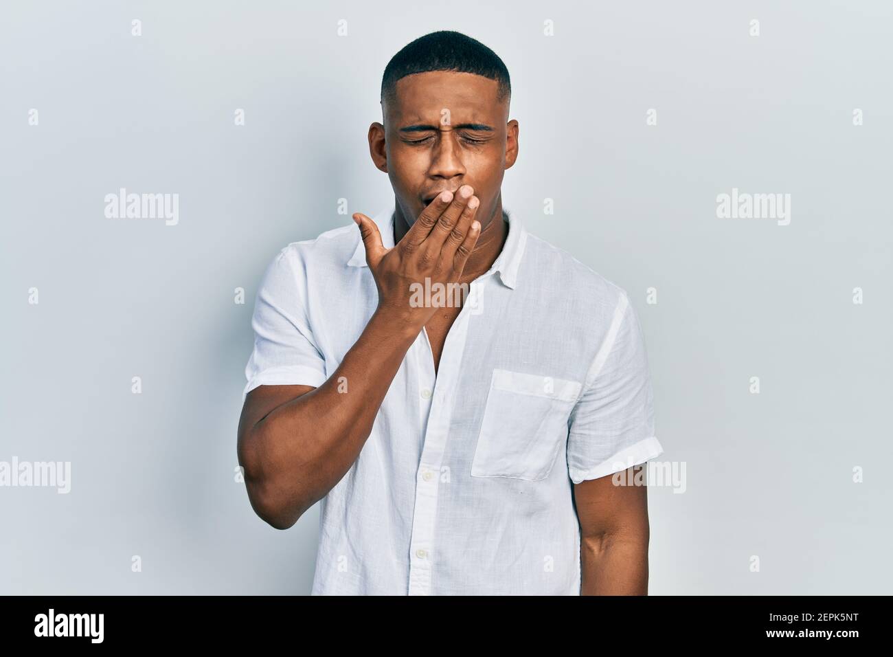 Young black man wearing casual white shirt bored yawning tired covering ...