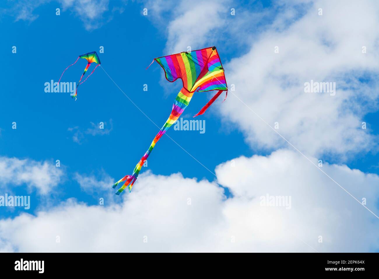Two colorful kites in a blue sky with white clouds - focus on the kite in the foreground Stock Photo