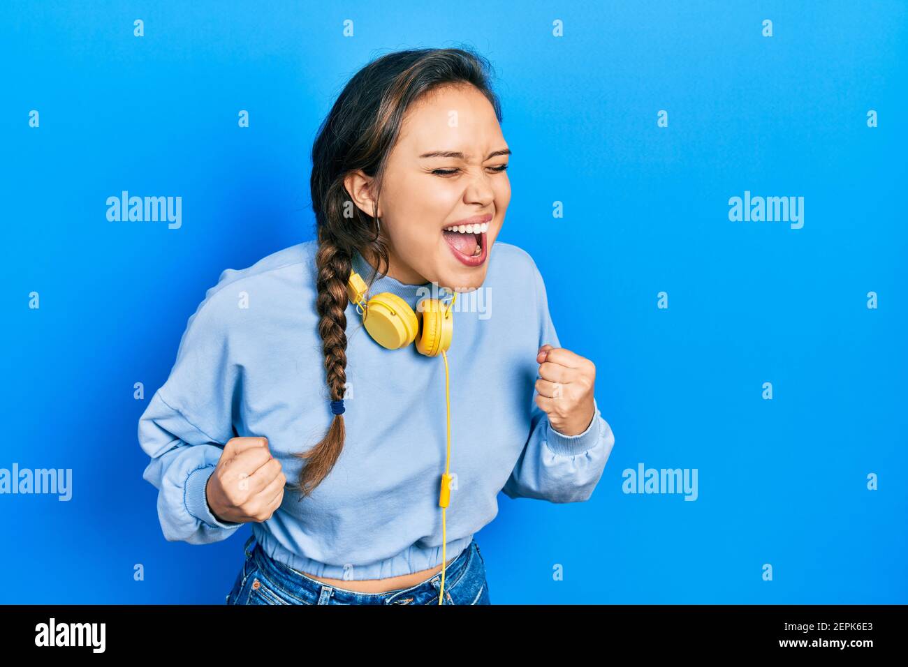 Young hispanic girl listening to music using headphones celebrating ...