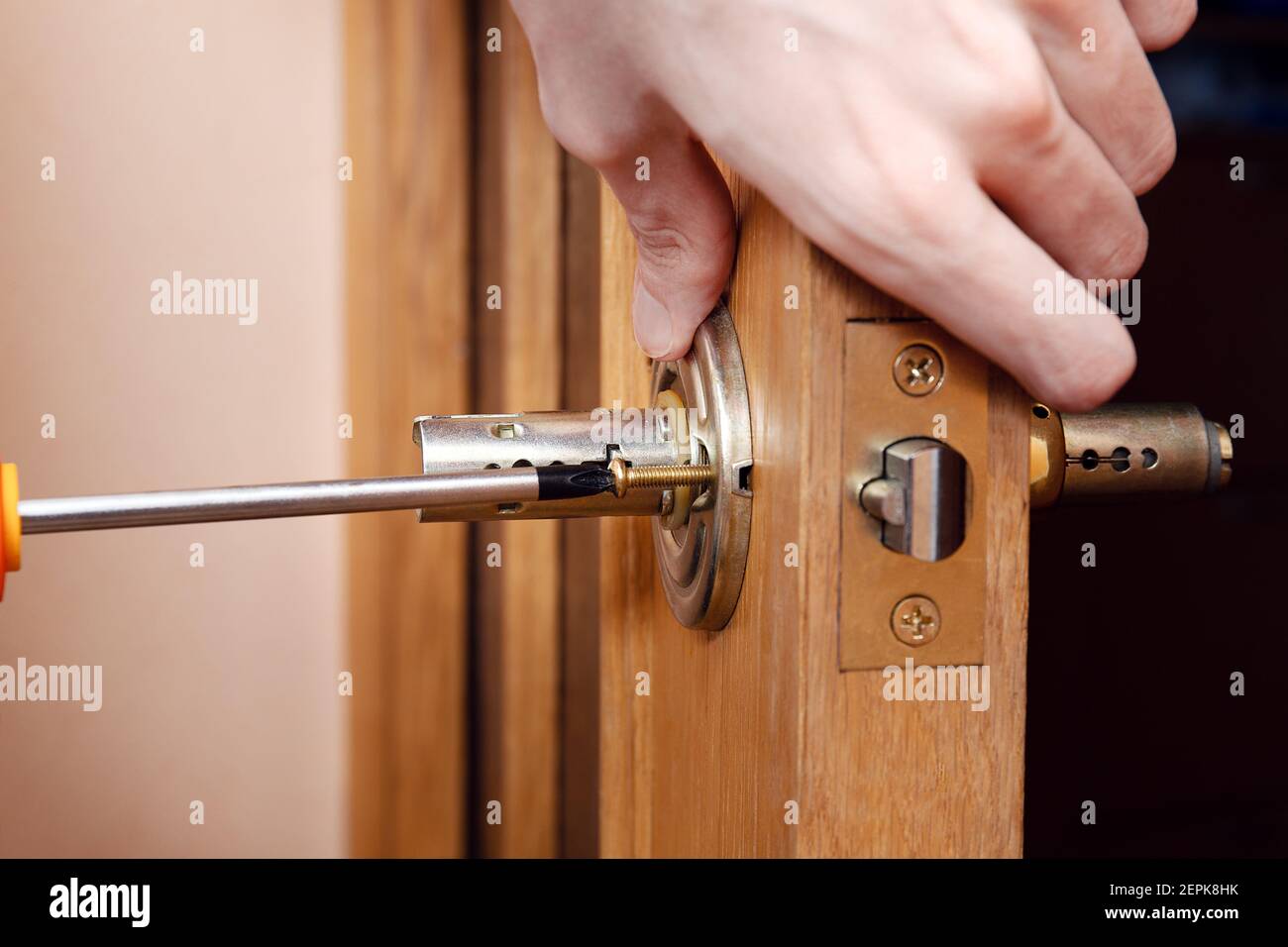 Door installation, worker Installs door knob, woodworker hands close up. A man spins the door handle with a screwdriver, repairs the door handle mecha Stock Photo
