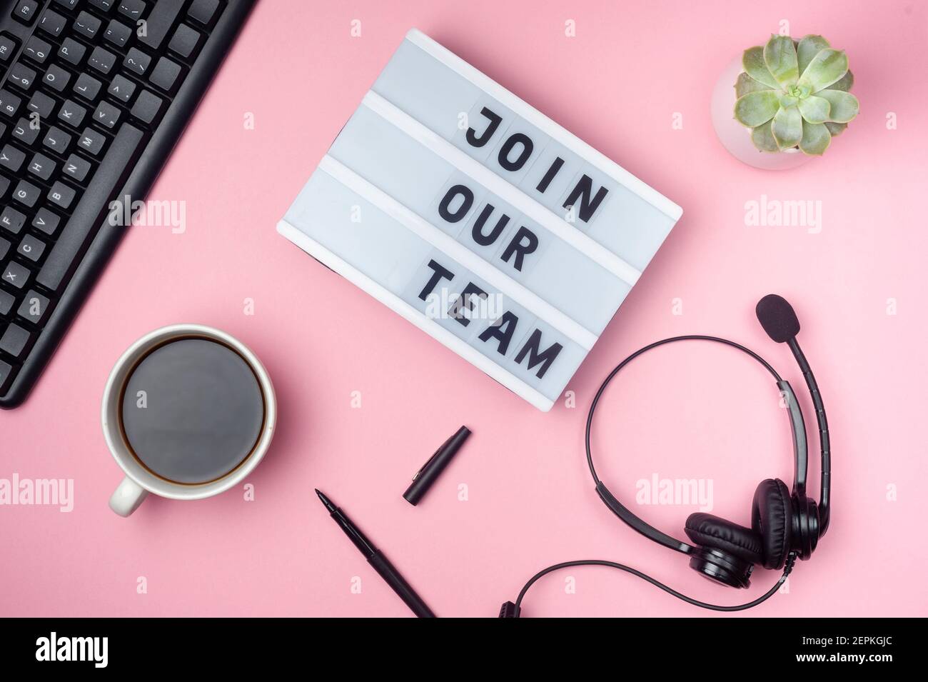 Join our team - text on display lightbox. Flat lay - keyboard, coffee, earphones and pen on pink background. Top view. Workplace concept. Stock Photo