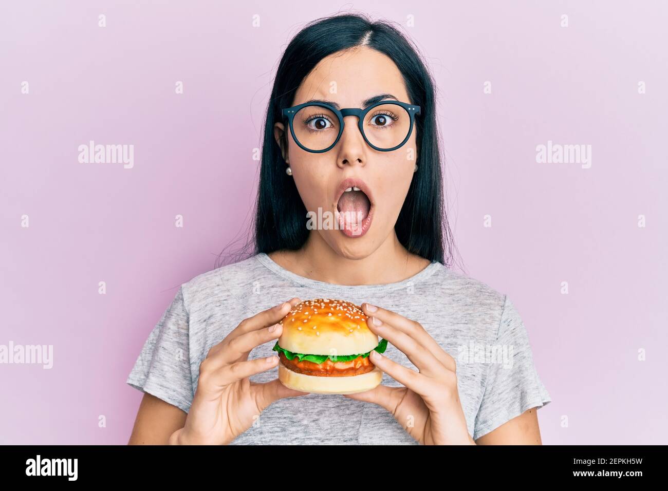 Beautiful young woman eating tasty hamburger afraid and shocked with