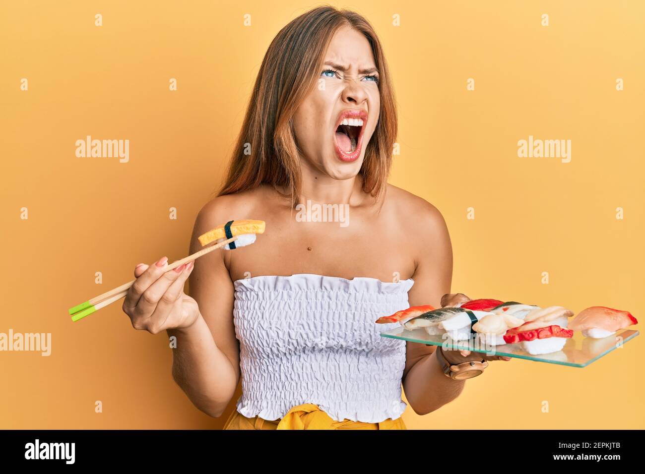 Beautiful young blonde woman eating omelette sushi using chopsticks ...