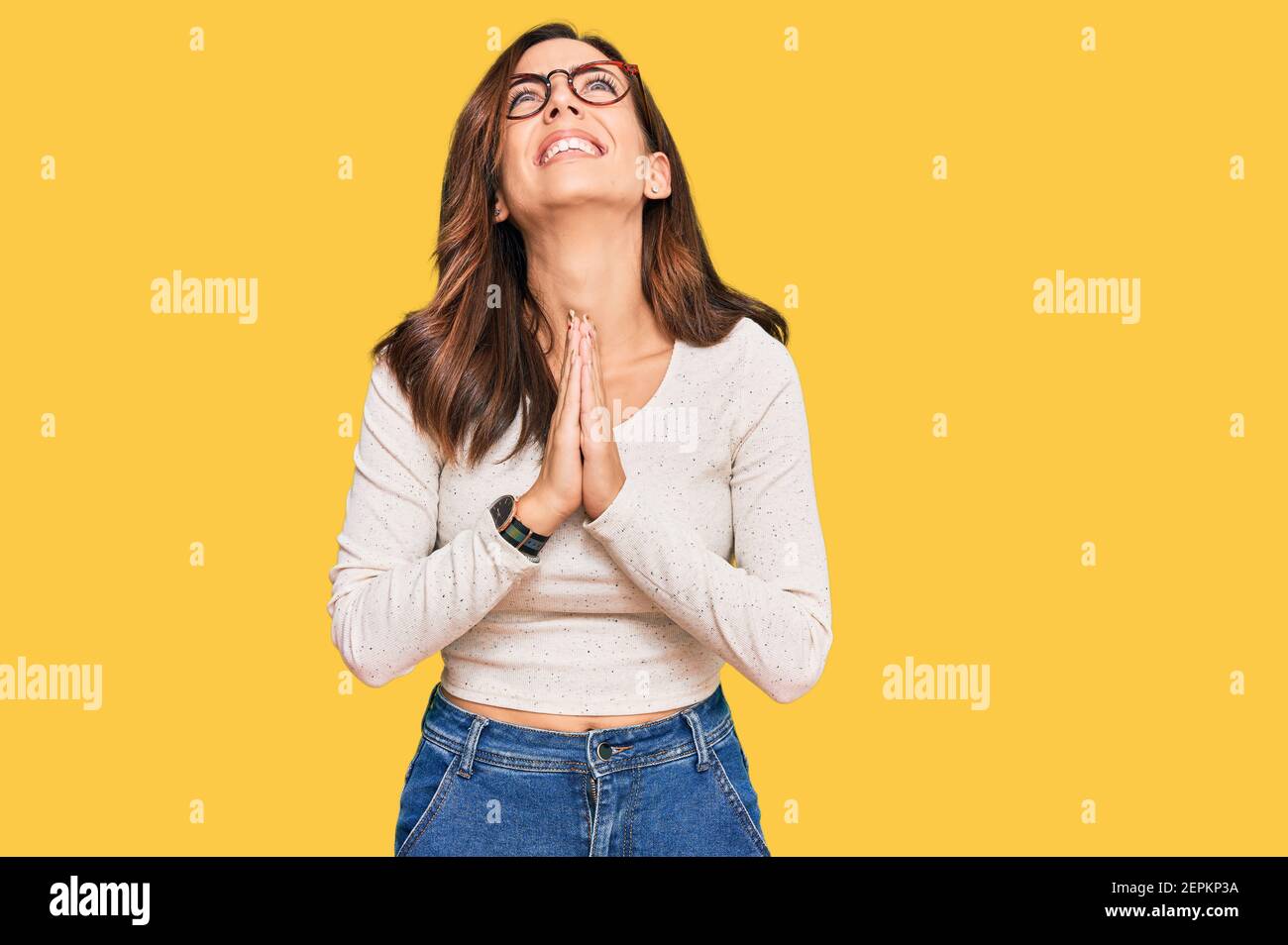 Young brunette woman wearing casual clothes and glasses begging and praying with hands together with hope expression on face very emotional and worrie Stock Photo