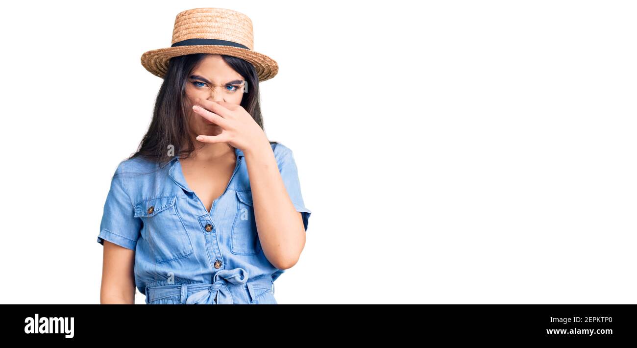 teenager girl wearing summer hat smelling something stinky and disgusting, intolerable
