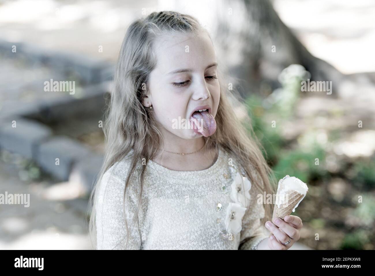 Kid girl with ice cream cone in hand. Summer treats concept. Sweet tooth girl child with white ice cream in waffle cone. Girl sweet tooth on disgusted face eats ice cream, light background. Stock Photo