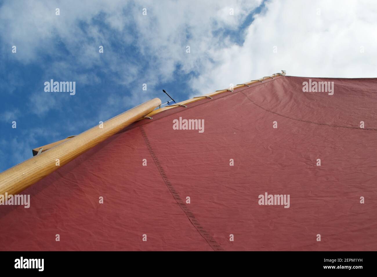 Looking up the rigging of a gaff rigged sailing dinghy: red lugsail sail, wooden mast, burgee and bright blue sky above Stock Photo