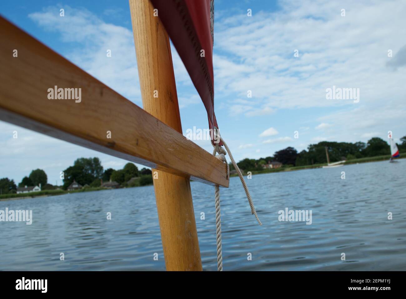 Close up of the wooden spar (boom) on a small sailing dinghy with a red sail, white ropes and wooden mast. Stock Photo