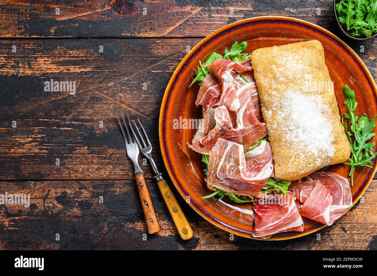 Spanish bocadillo de jamon, serrano ham sandwich on ciabatta bread with arugula. Dark wooden background. Top view. Copy space Stock Photo