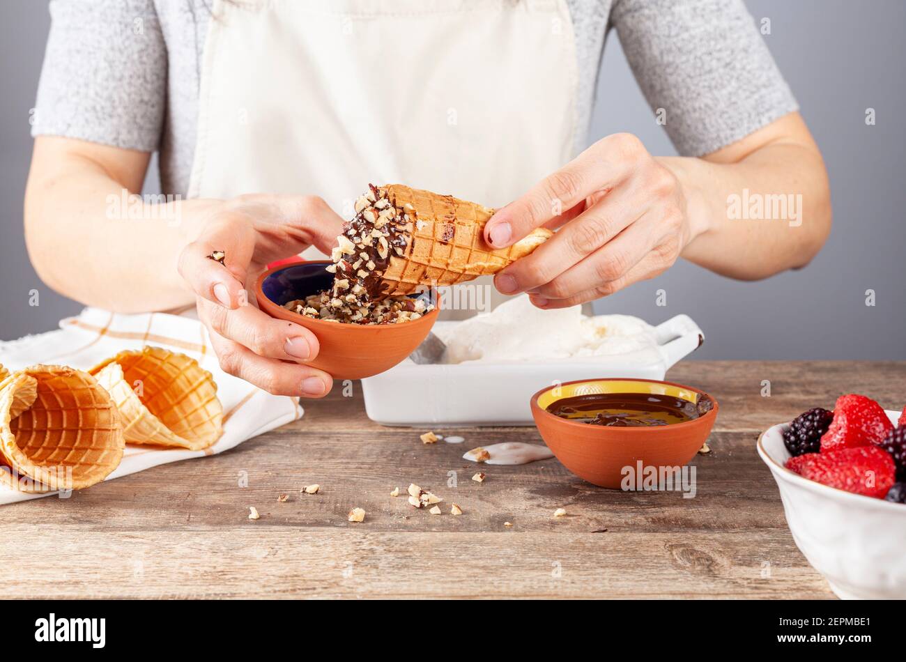 A woman chef is dipping homemade waffle ice cream cones into chocolate melt and walnut pieces for artisan look. Other hand rolled cones are there. A m Stock Photo