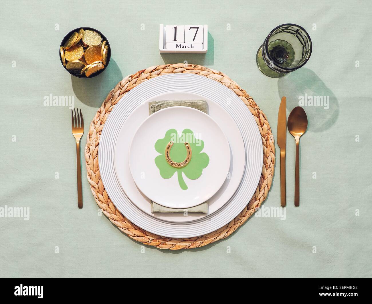 Beautiful festive table setting for St.Patrick's day with cutlery and lucky symbols. Top view of Saint Patrick's day holiday table with green linen tablecloth. Flat lay. Stock Photo