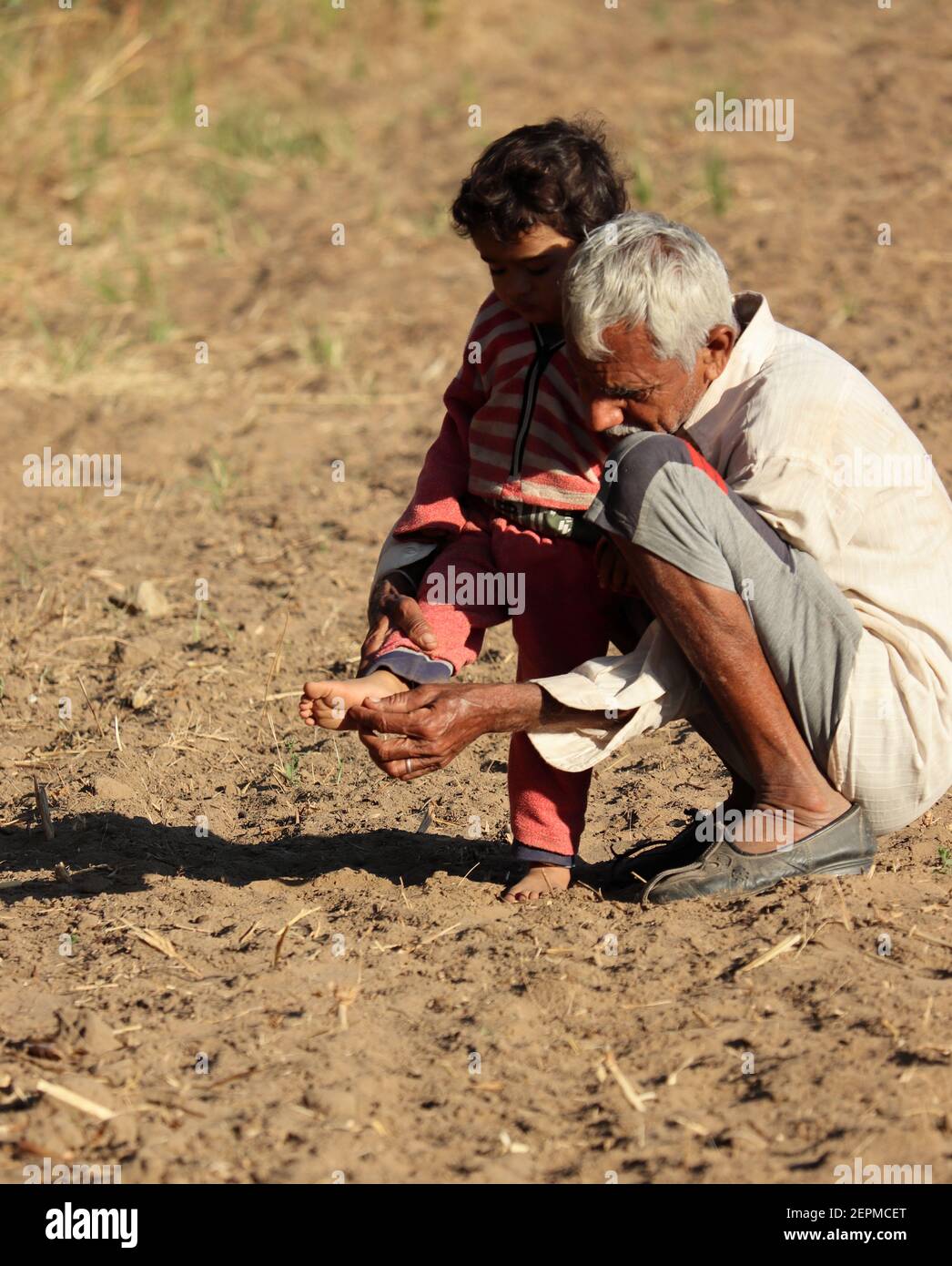 An Indian grandfather emitting a prickling thorn under the foot of his little beloved grandson. , India . concept for India's past smiling child, chil Stock Photo
