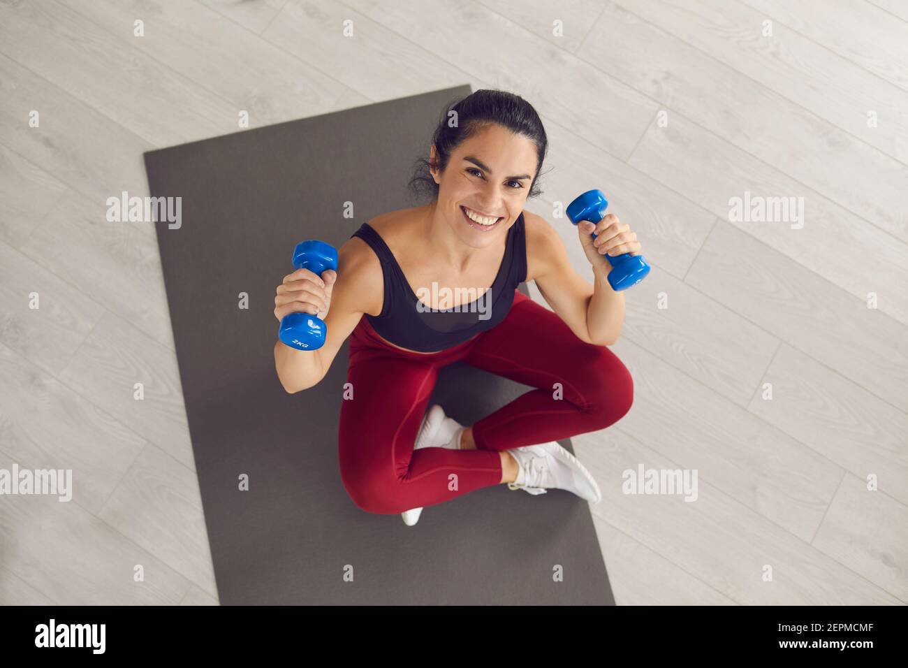 Smiling young fitness slim woman in sportswear sitting on mat and doing abs exercises Stock Photo